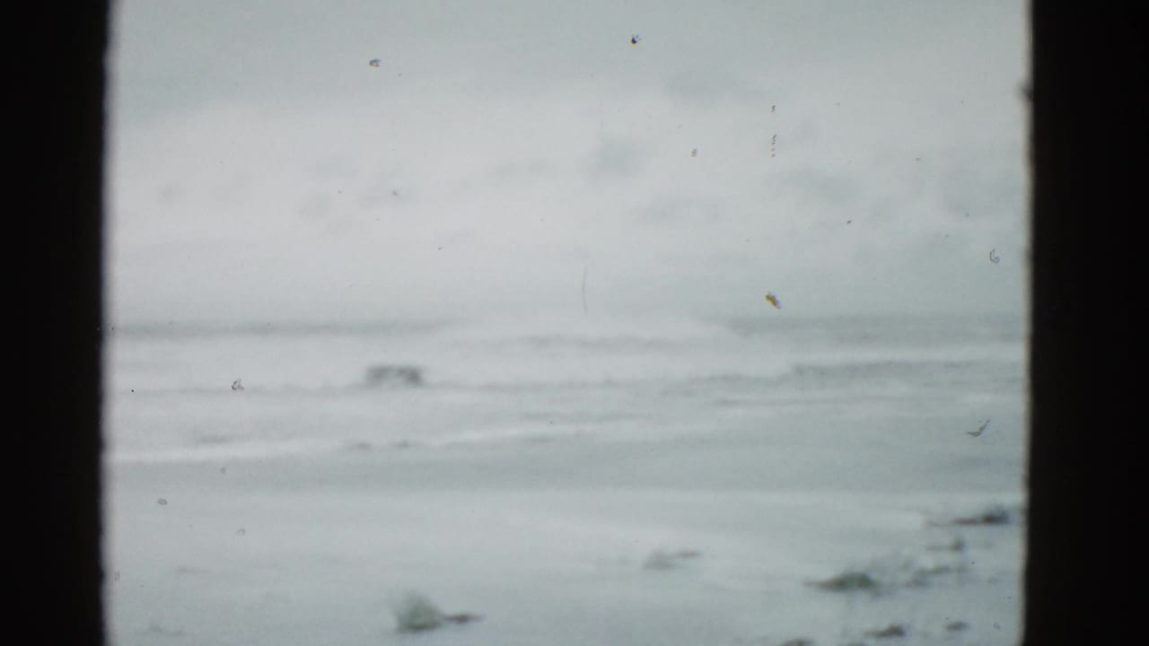 Cloudy surf and empty beach seen through dark vertical film borders.