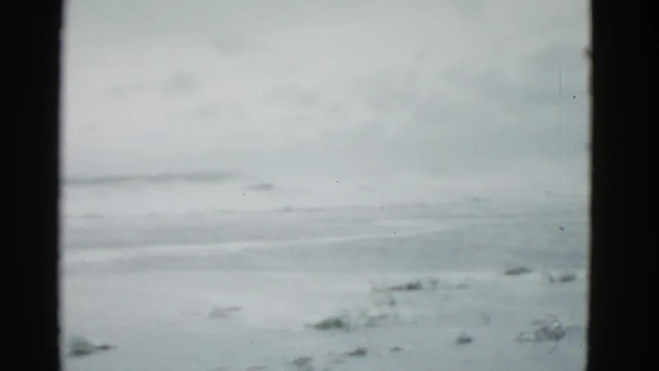 1975 Boston-area 8mm frame showing a frozen lake, low horizon, and overcast winter sky with visible film-gate edges.