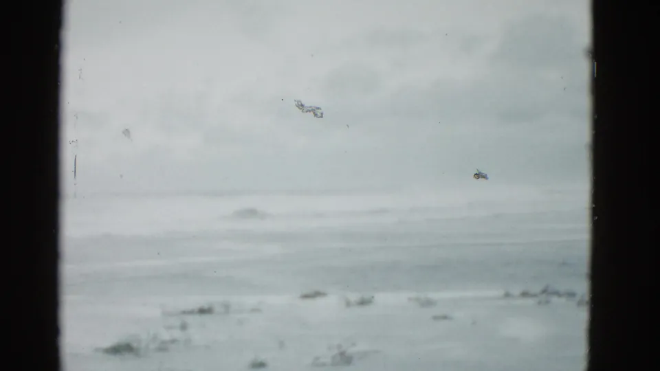 1975 Boston-area 8mm frame showing a frozen lake and pale sky, with dust, scratches, and soft exposure from the film scan.