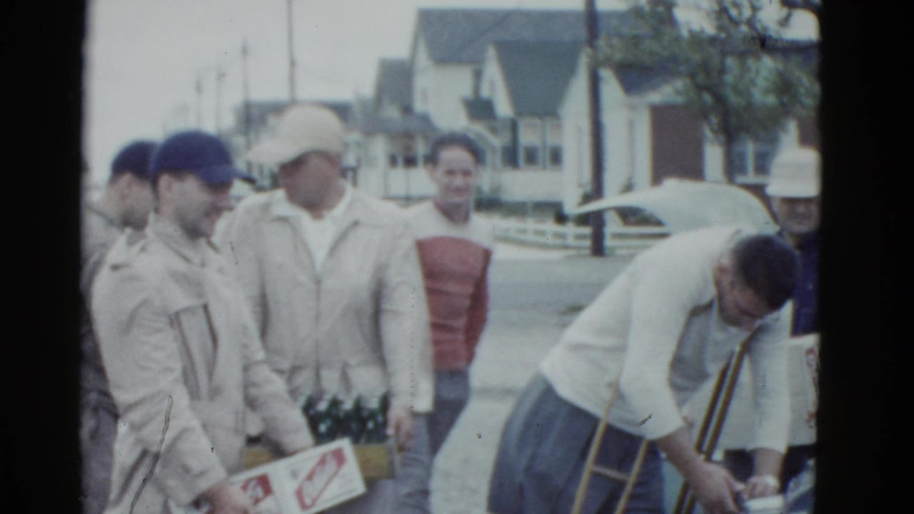 Men stand beside a car with Ortlieb's beer boxes on a residential street.