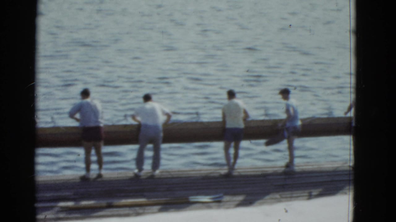 Men stand along a dock with a long log at the lake edge.