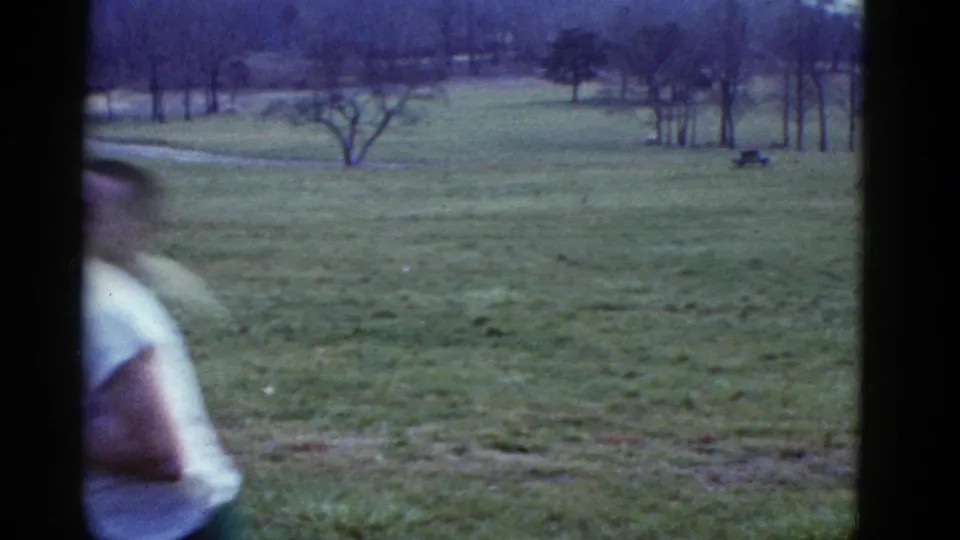 A runner passes the lens in a 1975 Boston-area cross-country scene, with open grass and leafless trees behind him.