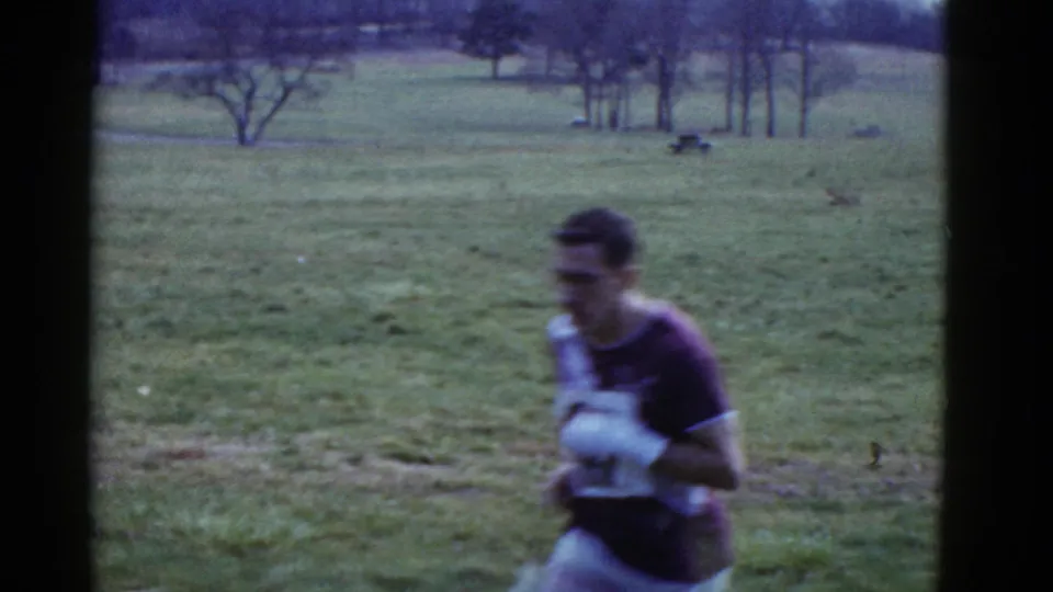 Close handheld 8mm frame of a runner passing the camera during the 1975 Boston-area field race.