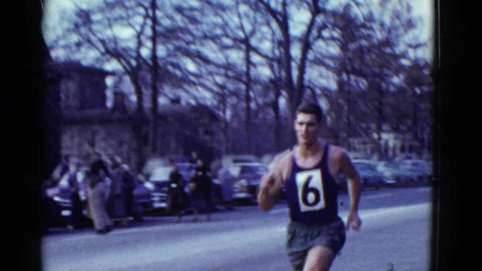 1975 Boston-area street-race frame showing a runner with bib number 6 passing parked cars and onlookers.