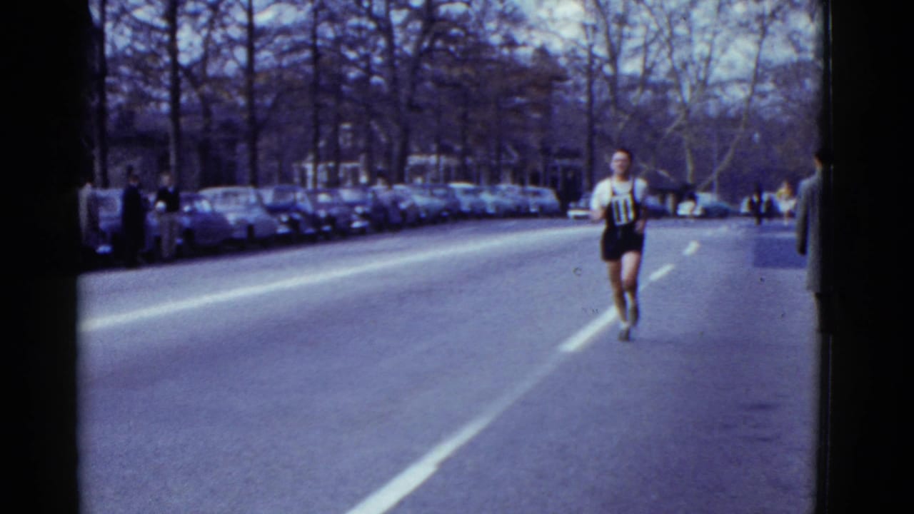 Runner with bib 11 approaches on a tree-lined city street with parked cars.