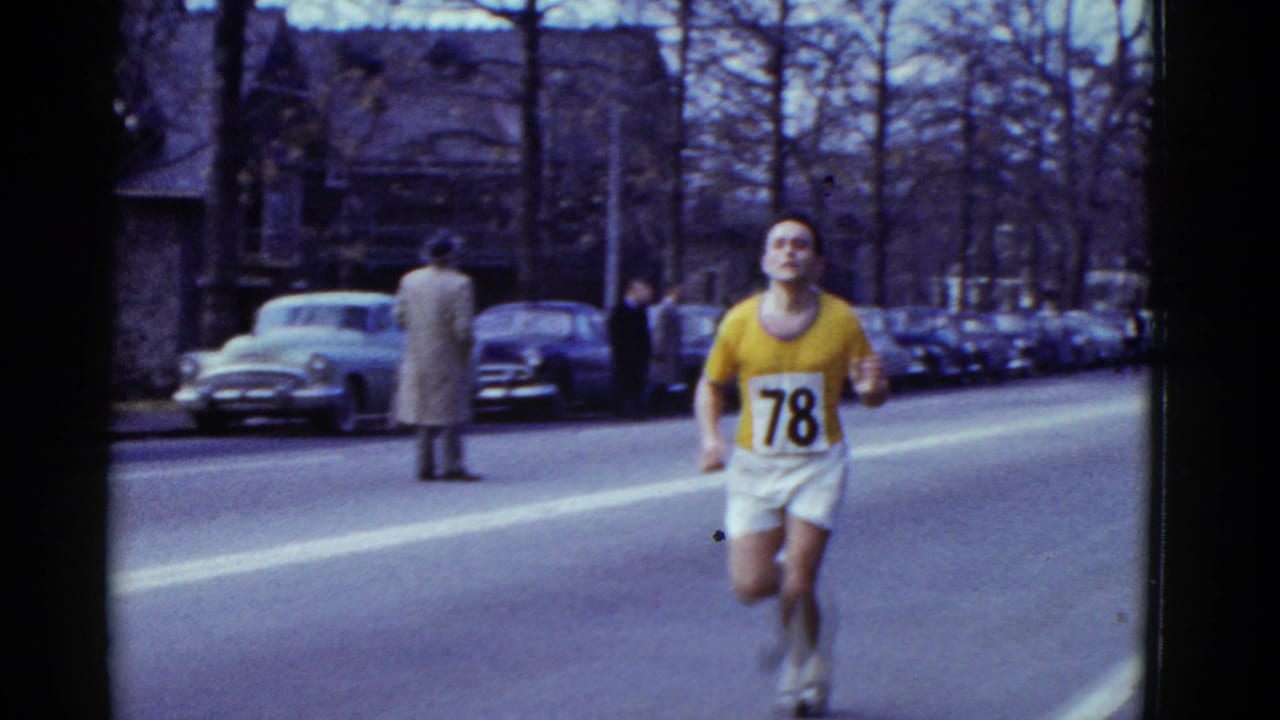 Runner in yellow shirt with bib 78 runs down a city street past parked cars and spectators.
