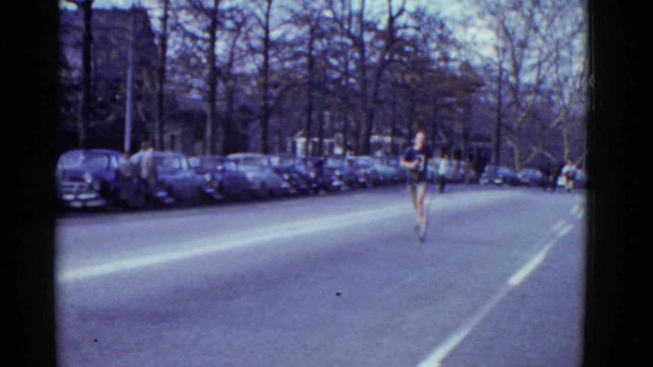 Distant runner on a wide street with parked cars and bare trees along the curb.