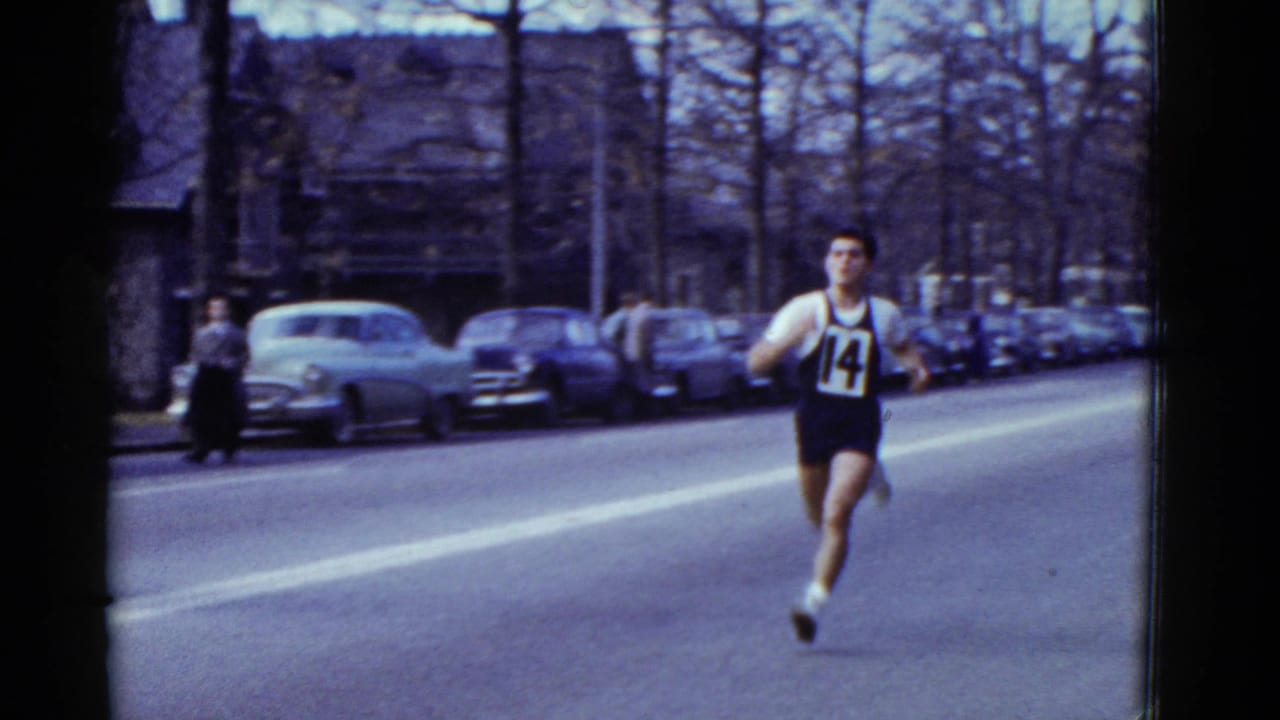 Runner wearing bib number 14 moves along a closed street lined with parked cars.