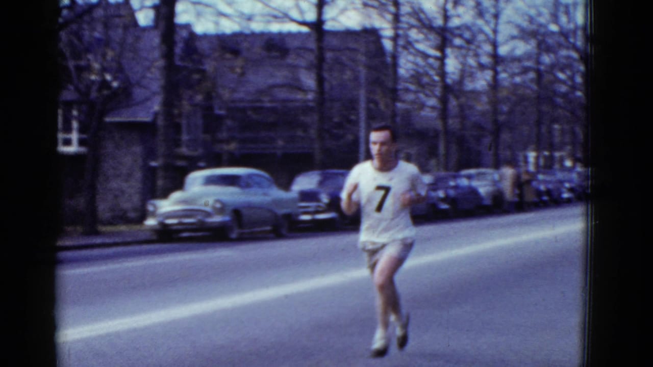 A male runner wearing number 7 is closer in frame on a Boston residential street, with mid-century cars and bare trees behind him.
