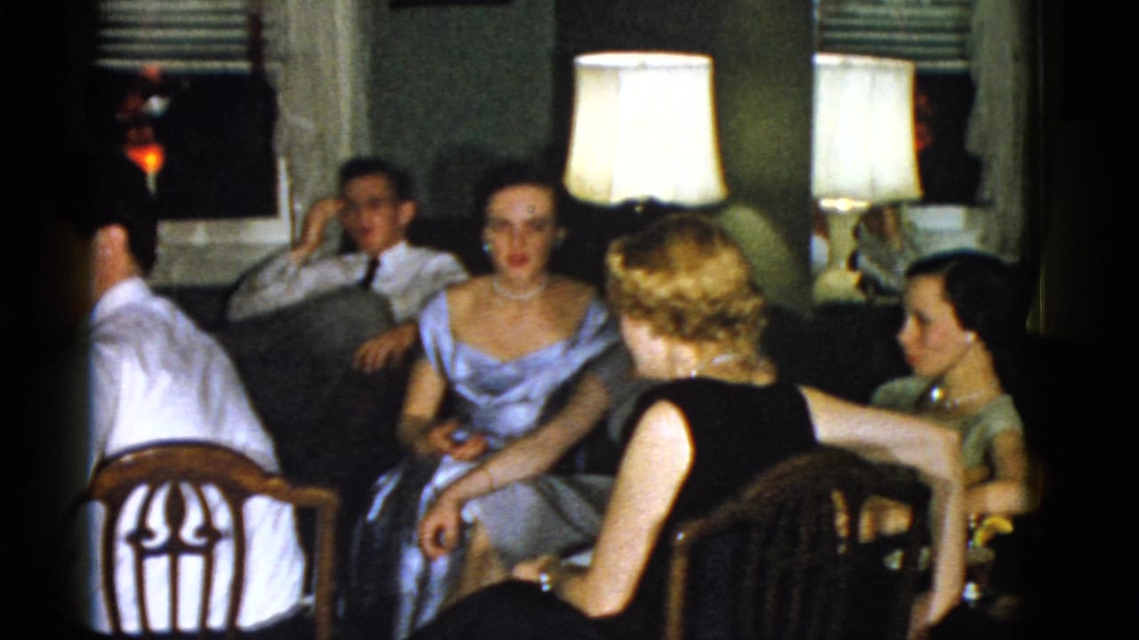 1975 Boston home-movie view of adults gathered in a private living room, with a woman turned toward the group.