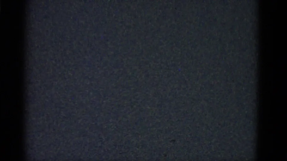 Underexposed 8mm frame from the Boston 1975 clip, with mostly dark image area and faint film grain below the prior interior scene.