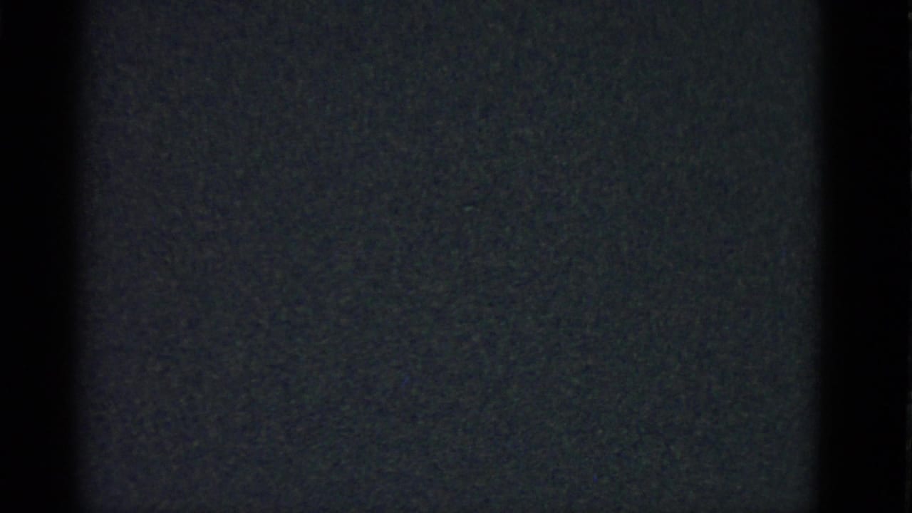 Grainy 8mm frame from the 1975 clip showing mostly black static with faint vertical tonal bands.