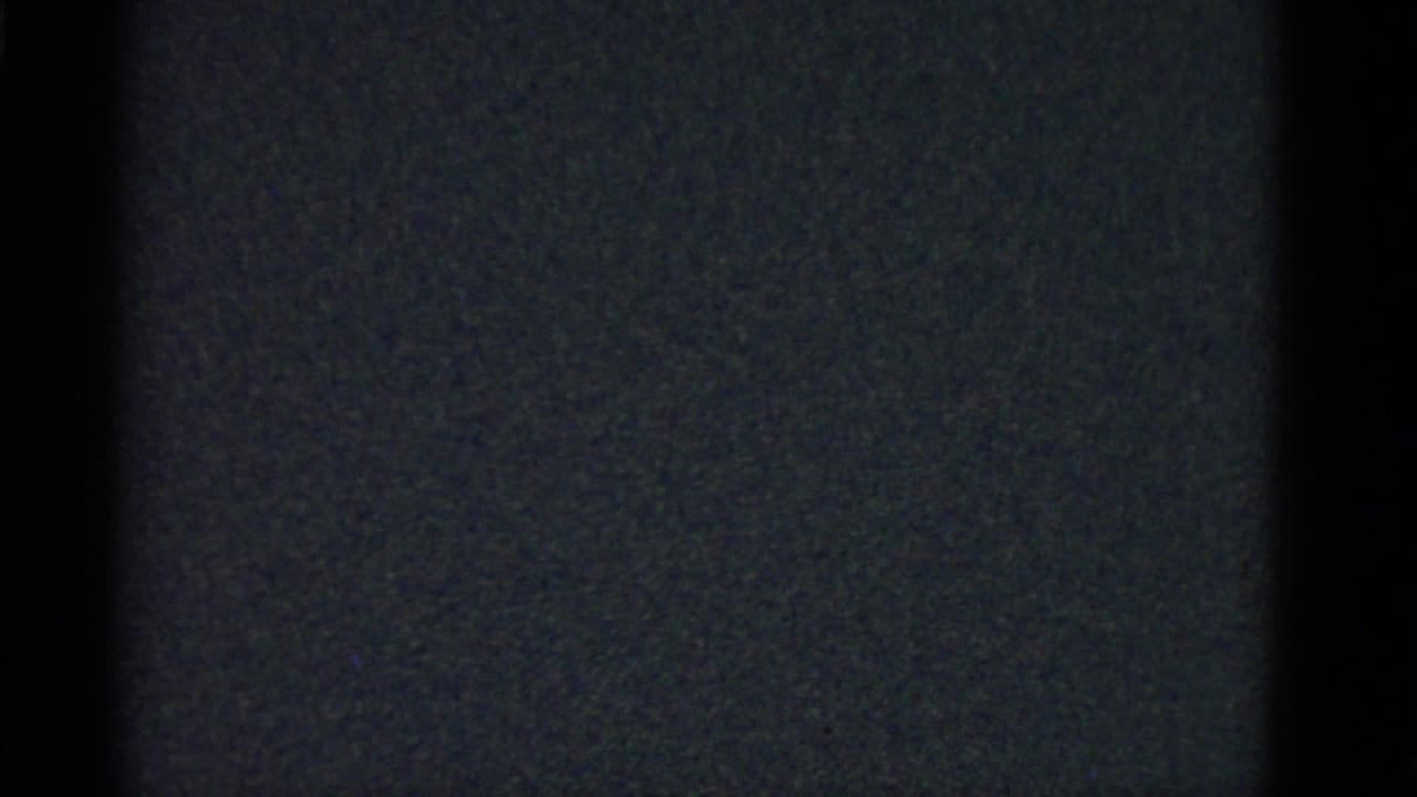 Underexposed 8mm frame showing dark static-like texture before the interior scene becomes visible.
