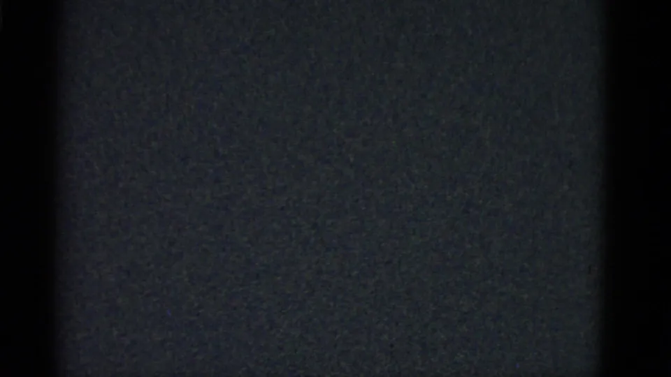 Underexposed 8mm frame showing dark static-like texture before the interior scene becomes visible.