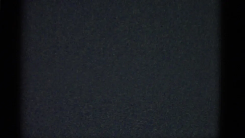 1975 Boston 8mm frame showing a young man in a light collared shirt facing others in a dark interior.