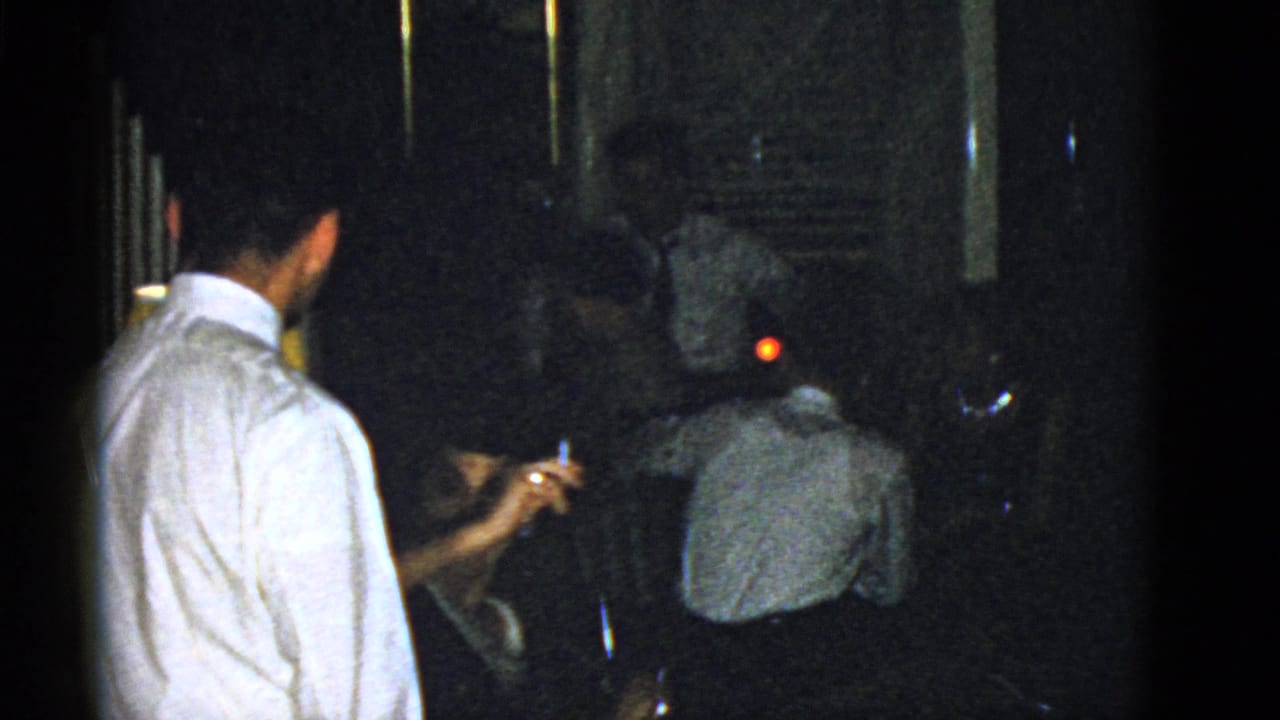 A seated woman raises a cigarette while a man in a white shirt and other guests occupy the dim 1975 Boston interior.