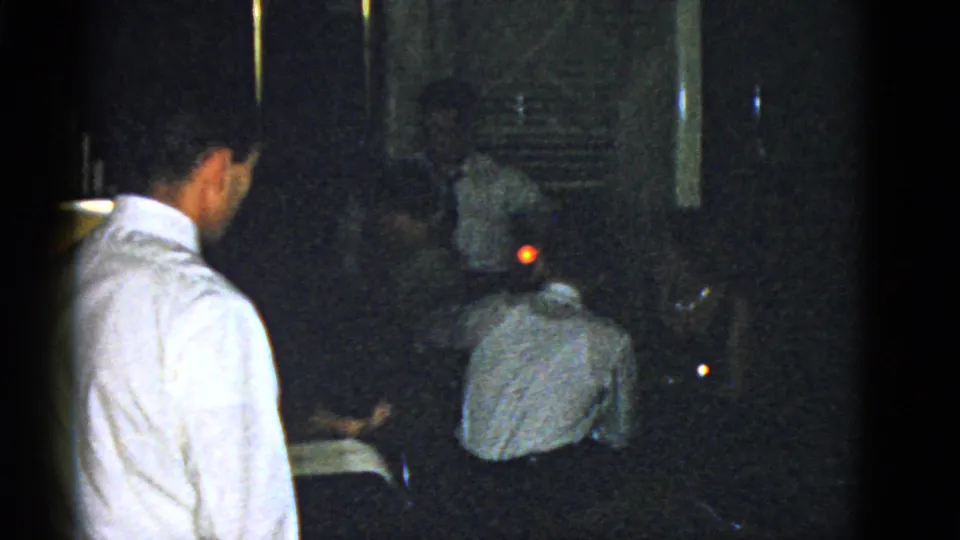 The closing frame shows adults seated and standing in the dim Boston interior, with a small orange light near the background.
