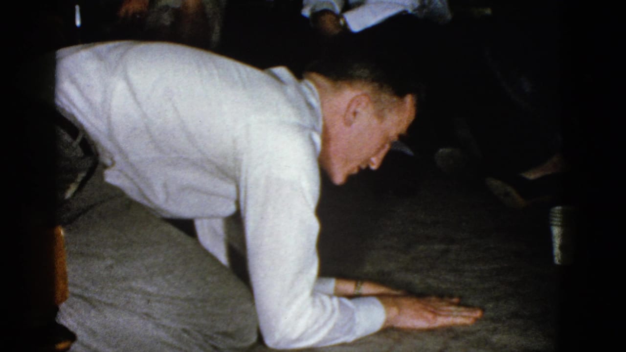 Man kneels with both hands near the floor while a paper cup sits in the background.
