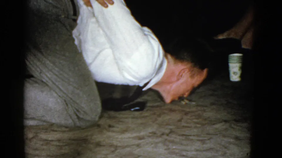 In the final 1975 Boston frame, the man bends very low while kneeling, his face close to the floor, with a paper cup and seated legs nearby.