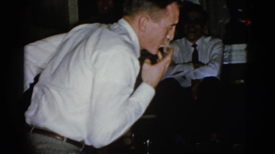 In the final frame, the man appears to lift a straw with his mouth as a smiling man in a shirt and tie watches from the background.