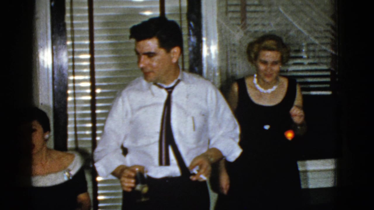 Man in a white shirt and tie holds a drink near party guests.
