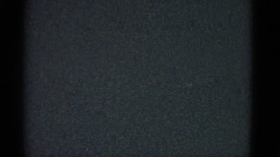Dark 1975 8mm frame from Boston metadata, showing vertical black bands, grain, and a faint blue-gray film field.