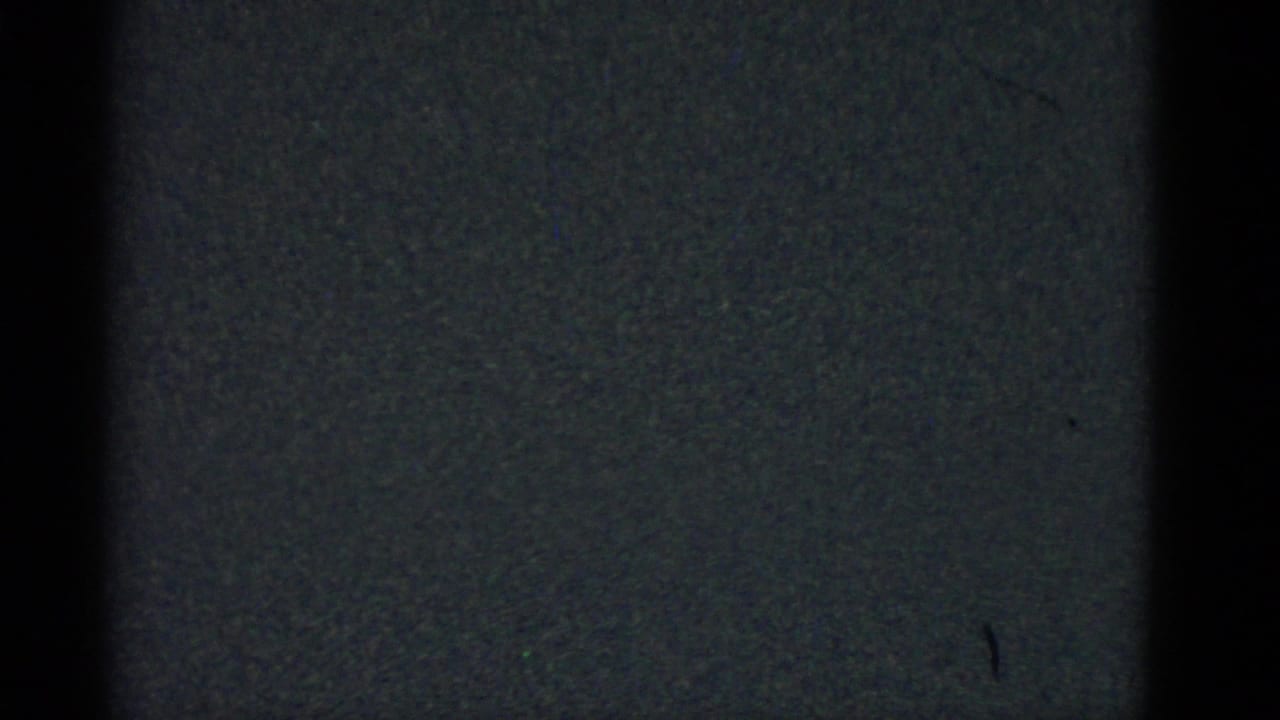 Dark 1975 8mm frame from Boston metadata with grain, a central black band, and a small visible mark on the right side.