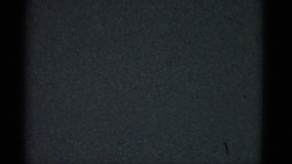 Dark 1975 8mm frame from Boston metadata with grain, a central black band, and a small visible mark on the right side.