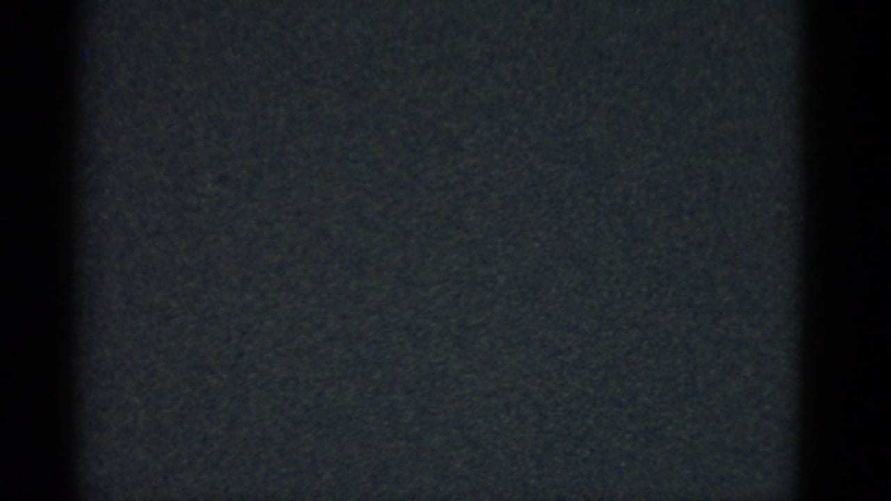 Dark 8mm frame with grain and a central vertical border, with no clear person or object visible.