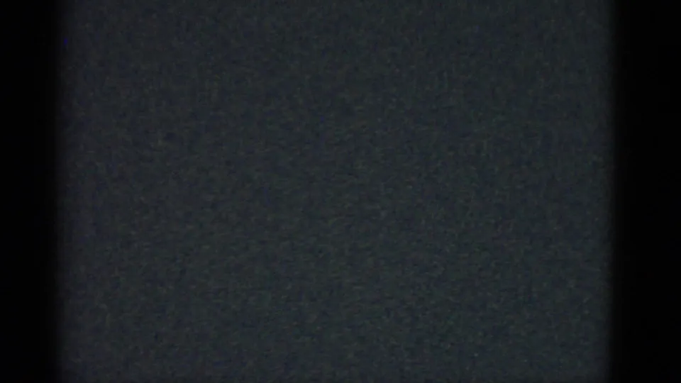 Dark 8mm frame with grain and a central vertical border, with no clear person or object visible.