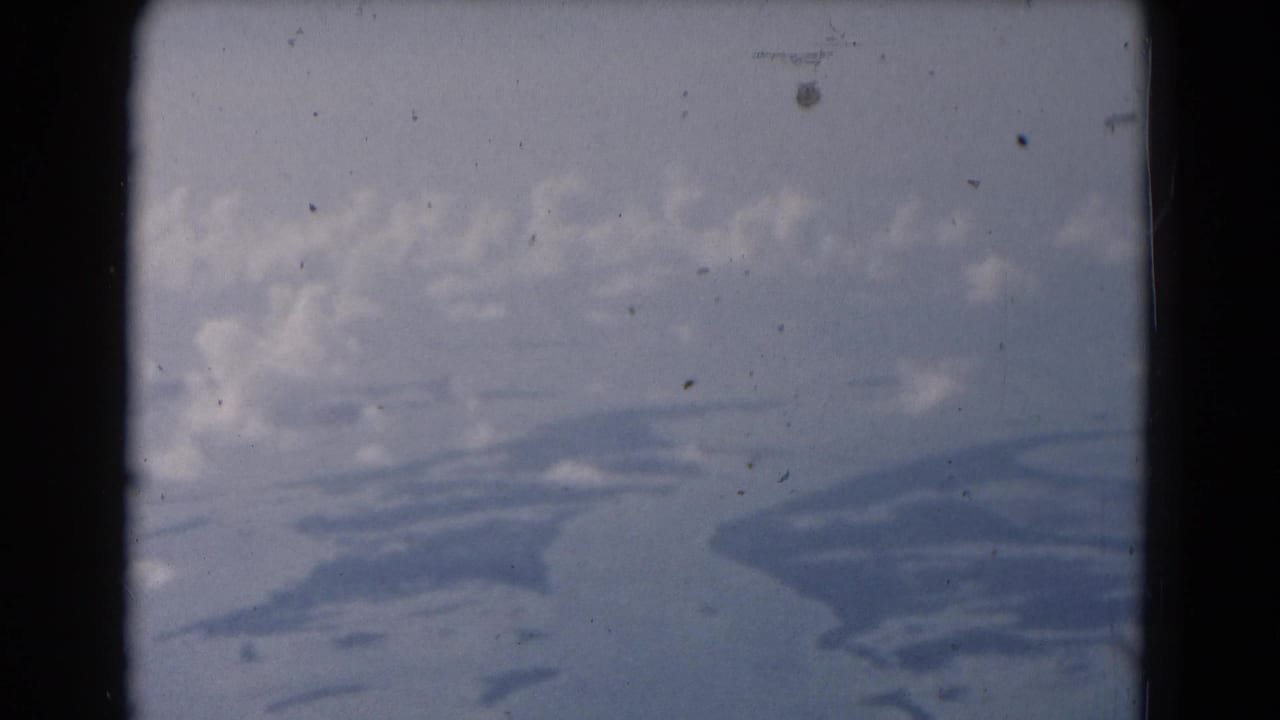 Damaged film frame with cloudy sky, dark gate edges, and soft blue-gray shapes below.