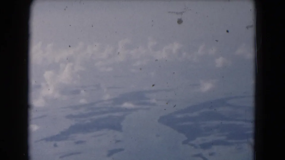 1975 8mm Florida home-movie frame showing a cloudy sky through damaged film edges, with indistinct blue-gray shapes below.