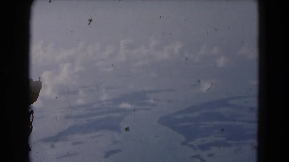 Soft 8mm frame from the Florida clip with overcast sky, dust marks, and indistinct shapes seen before the street view appears.