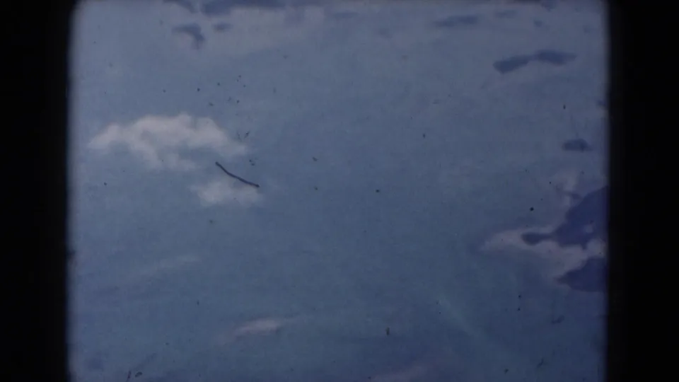 1975 Florida home-movie frame with overcast sky and blurred blue-gray lower shapes, affected by dust and heavy film-edge shadow.