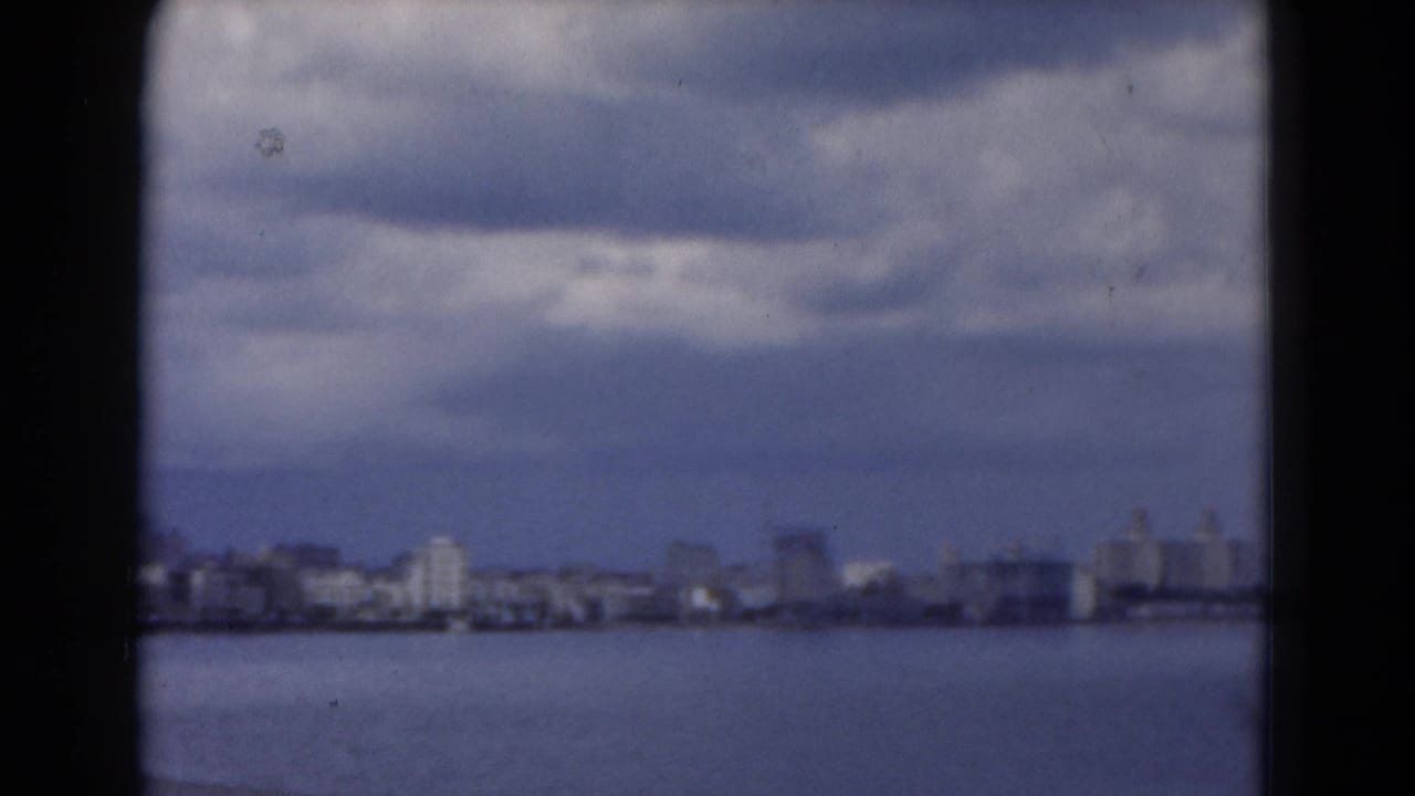 Distant city skyline across water beneath a cloudy sky.