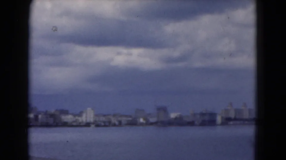 Soft 8mm view of a Florida waterfront skyline across open water under layered clouds.