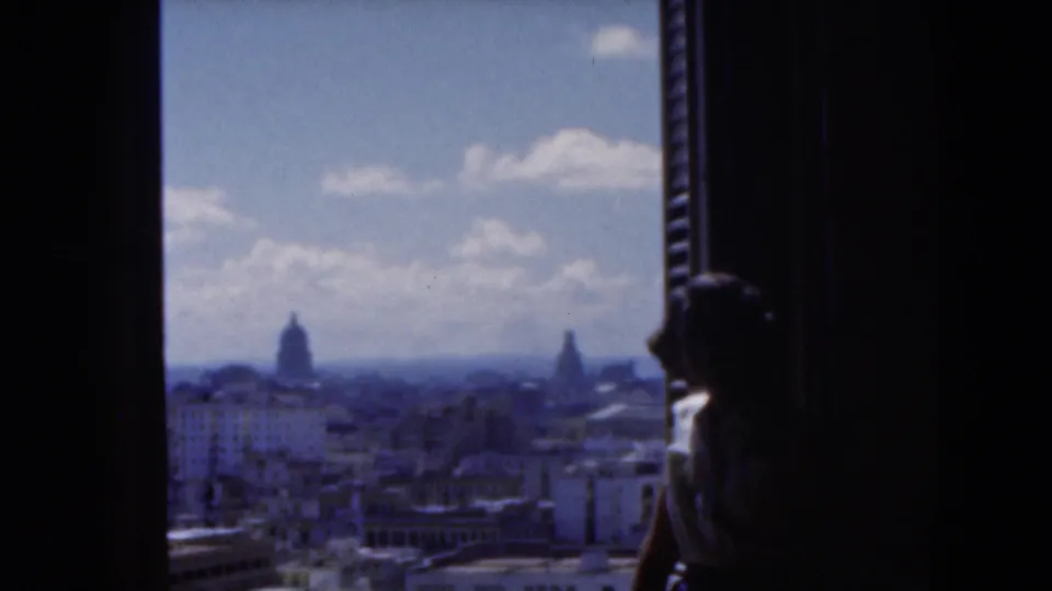 1975 Florida home-movie frame with a silhouetted person at an overlook facing a distant cityscape with domed buildings.