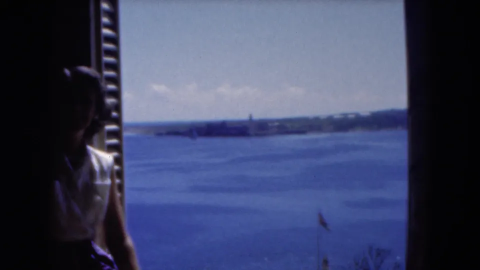 The 8mm frame shows a seated woman in shadow at the window edge, looking out across water in Florida.