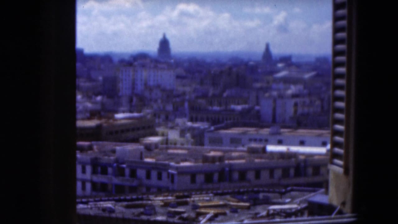 1975 Florida 8mm frame showing a hazy city panorama through dark shutters, with rooftops and distant domed structures under a bright sky.