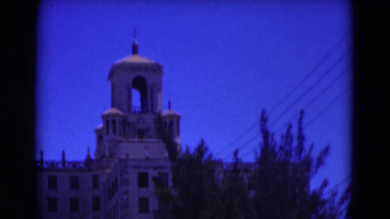 1975 Florida 8mm frame showing the upper tower and roofline of a large historic-looking building partly obscured by trees.