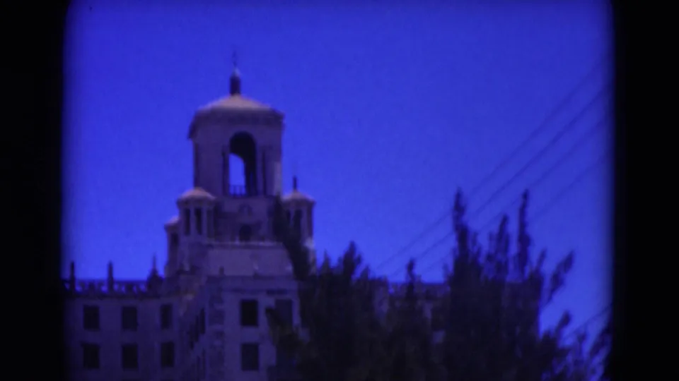 1975 Florida 8mm frame showing the upper tower and roofline of a large historic-looking building partly obscured by trees.