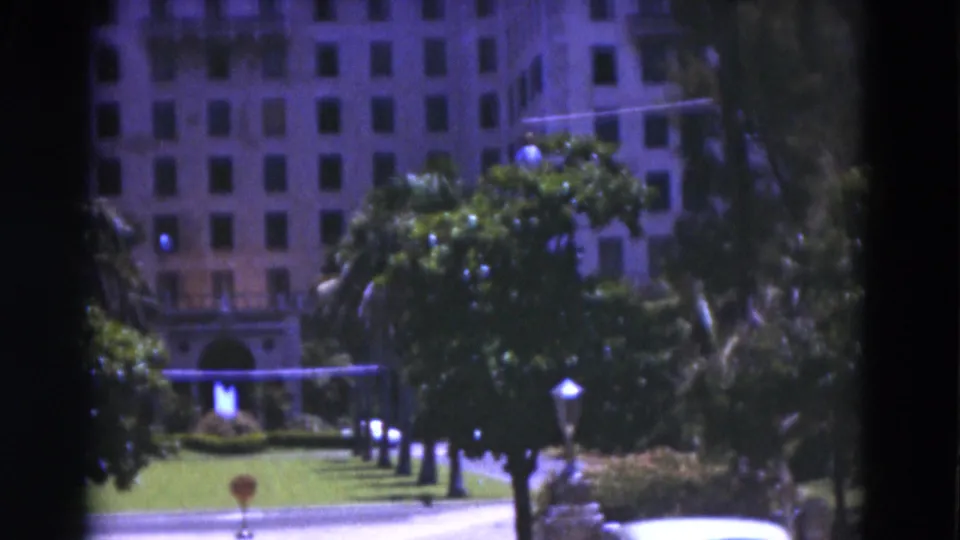 1975 Florida 8mm frame showing a green lawn, small lamps, trees, and an arched entry at the base of a large building.