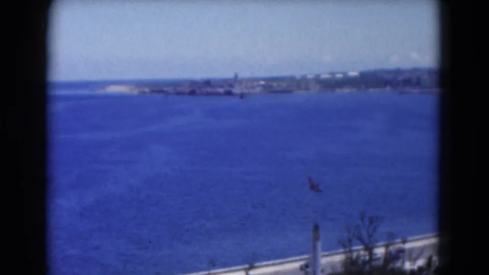 Florida 8mm coastal view showing deep blue water, distant shoreline, pale sky, and a flagpole near the lower edge.