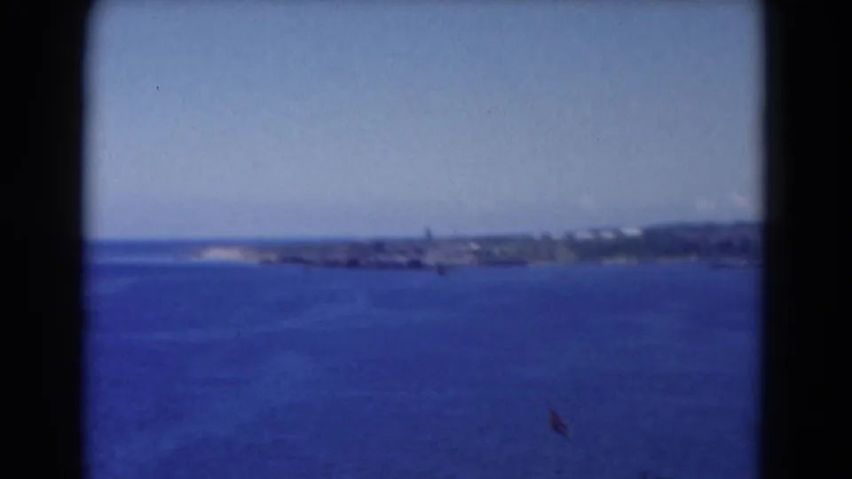 A coastal Florida view across blue water, with a low shoreline in the distance and visible 8mm frame borders.
