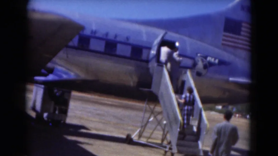 1975 Florida home-movie frame of passengers boarding a Pan Am aircraft by mobile stairs on a sunny outdoor airfield.