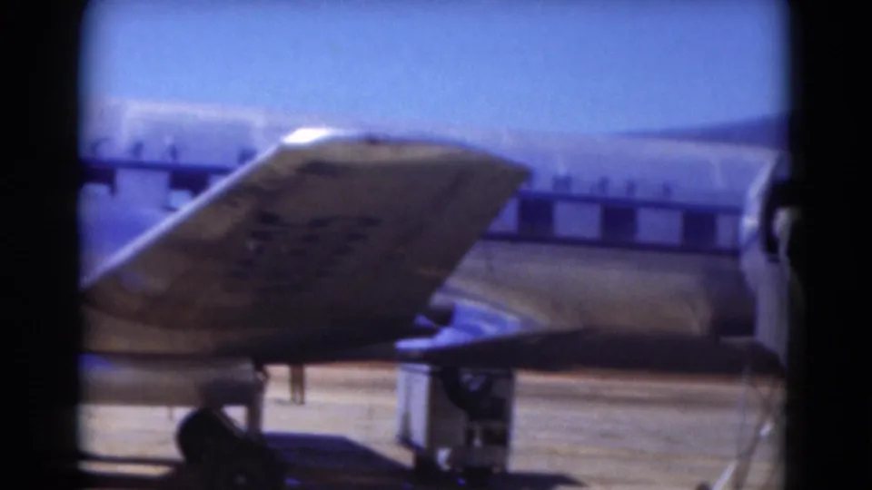 1975 Florida 8mm frame showing the rear section of a silver propeller airplane, with mobile stairs beside the fuselage.