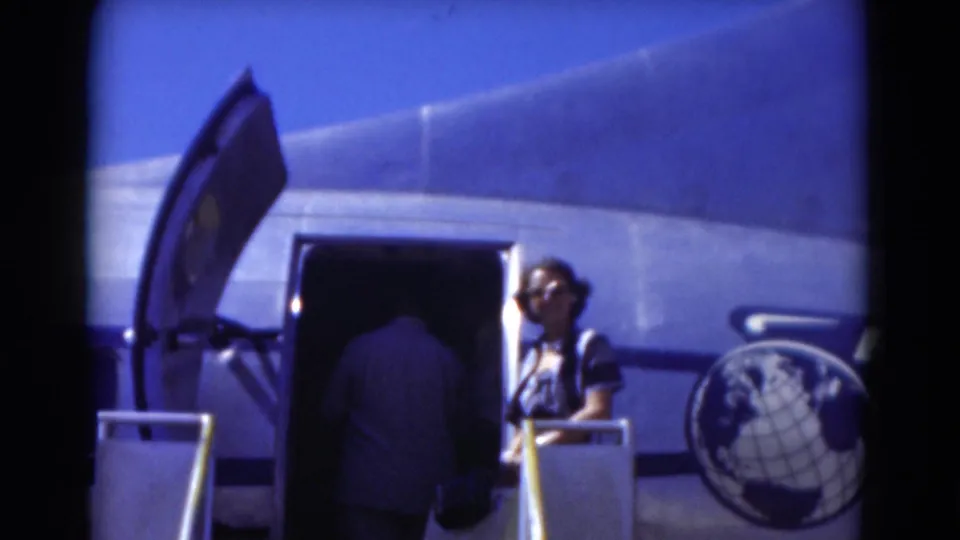 1975 Florida 8mm frame showing passengers boarding a silver propeller airplane through an open door on mobile stairs.