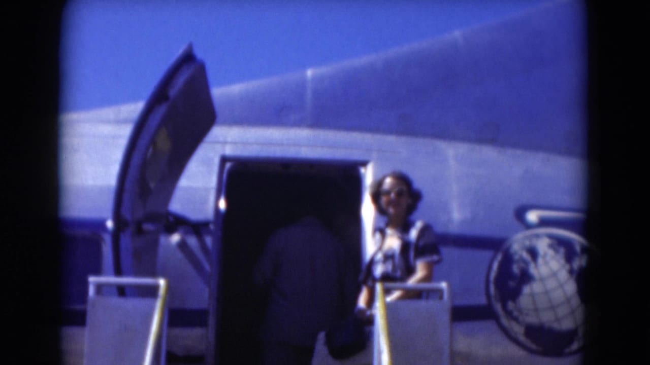 Woman stands beside an open aircraft door while a passenger boards from steps.