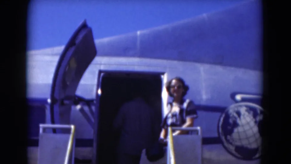 1975 Florida travel footage shows a woman in sunglasses near an open silver aircraft door as another passenger boards.