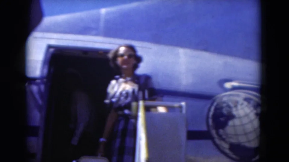 Close 8mm view of a woman in a striped dress and sunglasses standing beside the open aircraft doorway during the Florida trip.